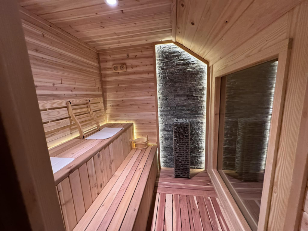 The interior of a modern cedar sauna built by Upstate Modern Builders LLC in Greenville, SC, featuring benches and a stone heater.