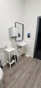 A newly installed modern commercial restroom with a wall-mounted sink, mirror, and grab bars by Fine Point Construction LLC in Medford, OR.