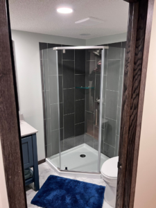 A modern corner shower with dark gray tiles and a white shower pan, part of a bathroom remodel by M.R. Renovations, LLC in Maple Grove, MN.