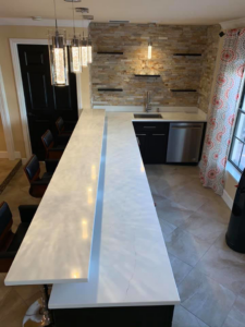 A modern custom bar installation featuring a long white countertop and pendant lights by Catalyst Contracting in Cape Coral, FL.