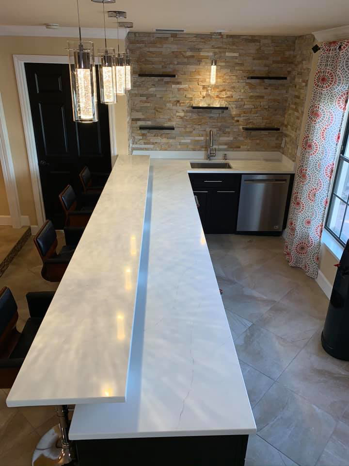 A modern custom bar installation featuring a long white countertop and pendant lights by Catalyst Contracting in Cape Coral, FL.