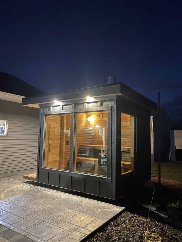 Modern dark grey sauna exterior at night, showcasing its design and lighting by No Boundaries Tiny Homes in Eau Claire, WI