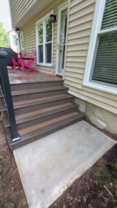 A modern deck with dark composite steps leading down to a concrete landing, installed by Deckscape KC in Kansas City, MO.