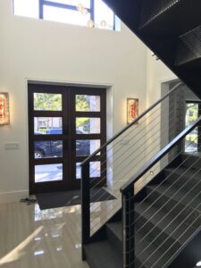 Modern entryway featuring a dark wood door and a sleek metal staircase by Charter Bay Home Builders in Tampa, FL