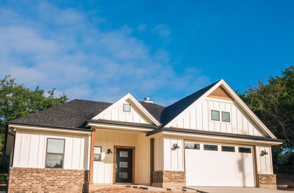 The exterior of a modern farmhouse style custom home with white siding and brick accents by Aubrey Homes in Austin, TX