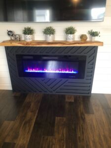 A modern fireplace with a geometric surround, wooden mantel, and mounted TV installed by The Huckleberry Handyman in Meridian, ID.