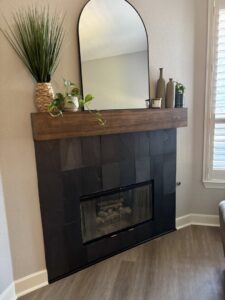 A newly renovated modern fireplace with dark tile and a wooden mantel by Riker Home Services in Plano, TX