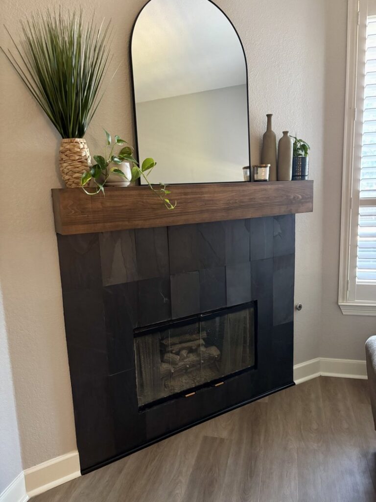 A newly renovated modern fireplace with dark tile and a wooden mantel by Riker Home Services in Plano, TX