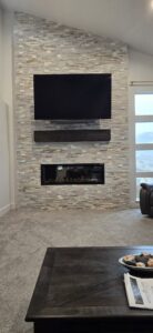 A modern stone veneer fireplace with a floating shelf and mounted TV, completed by Titan Handyman Services in Lewes, DE