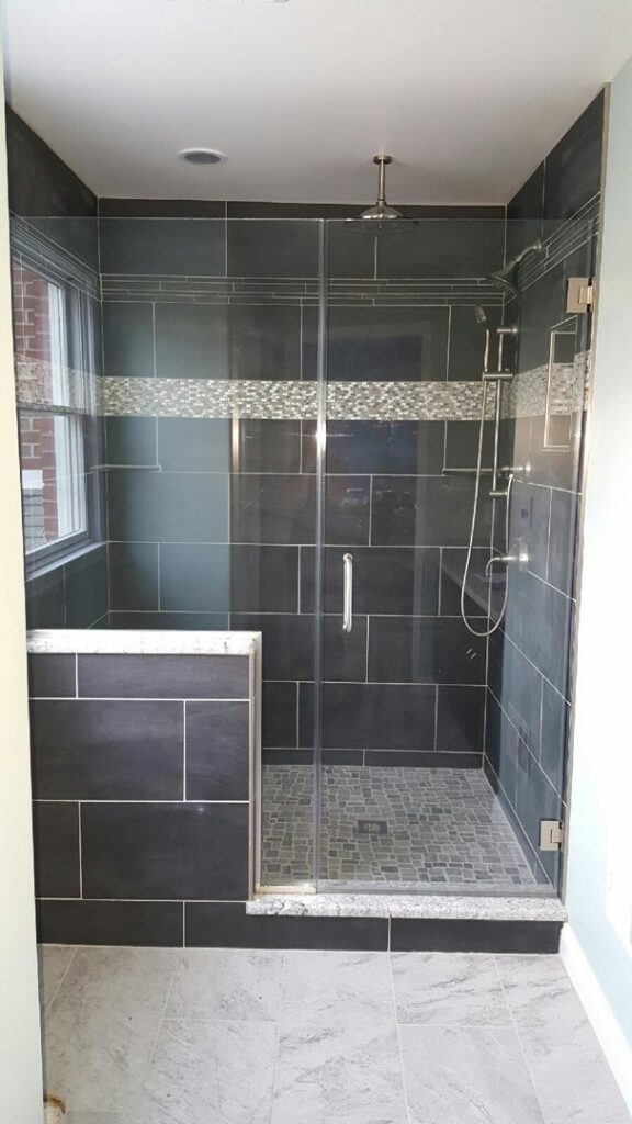 A modern frameless shower with dark tiles and a decorative band, installed by Lehigh Shower Glass in Bethlehem, PA