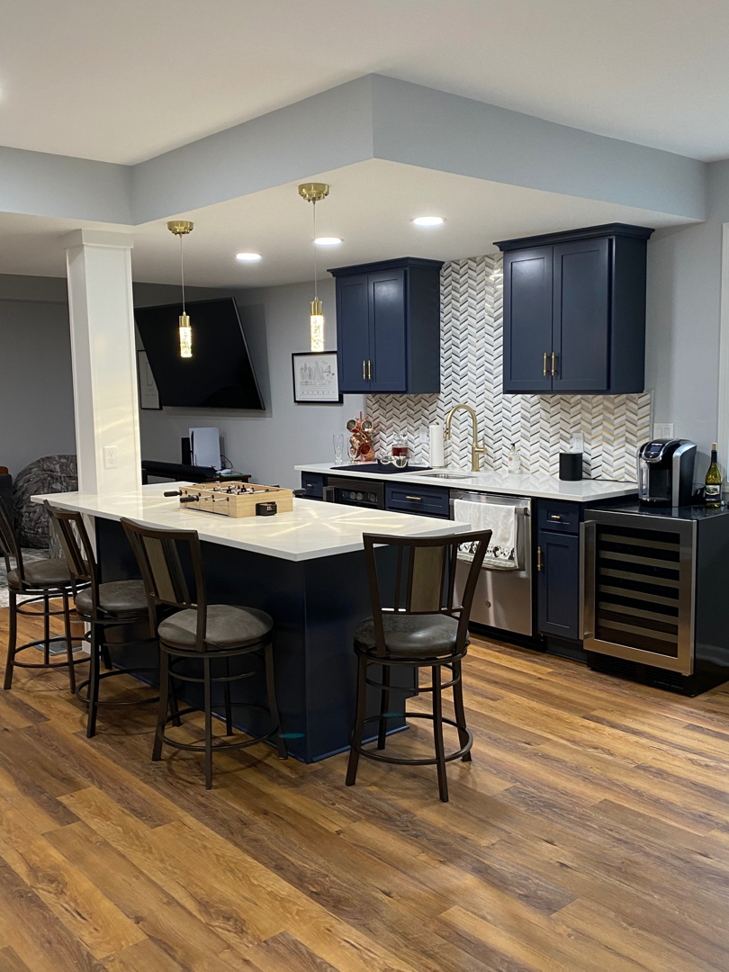 A modern kitchen and bar area renovation featuring dark blue cabinets, white countertops, and a tiled backsplash by Nader Builders in Ann Arbor, MI.