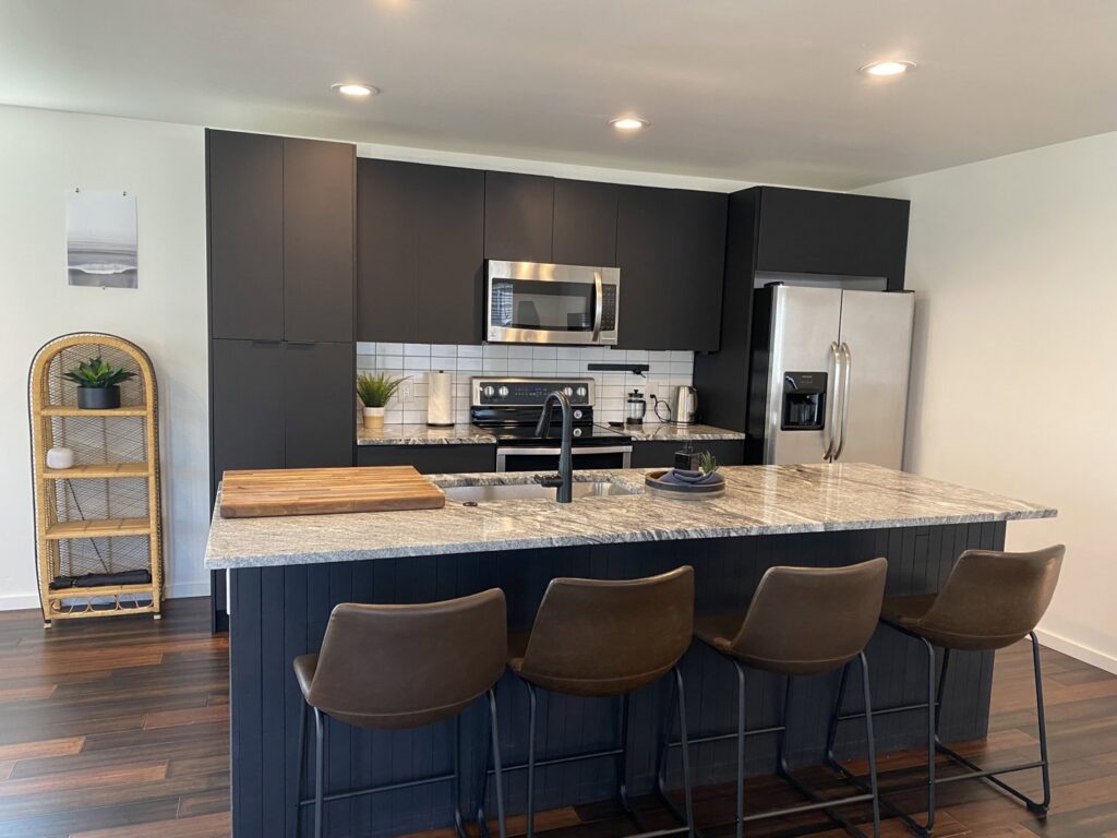 A sleek modern kitchen featuring black cabinets, stainless steel appliances, and a granite island by Pioneer Built in St. Petersburg, FL.