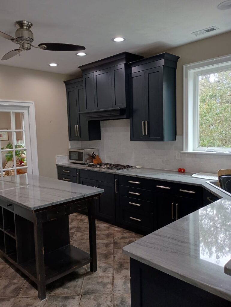 A modern kitchen featuring dark blue cabinets, white countertops, and stainless steel appliances by Coastal Surface Design in Virginia Beach, VA.