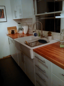 A modern kitchen featuring a farmhouse sink, wooden countertops, and white cabinets by Fine Hand LLC in Portland, OR