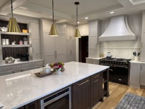 A modern kitchen remodel featuring light grey cabinets, a large island, and gold pendant lights by Saunders Dynamic Remodeling in Columbus, OH
