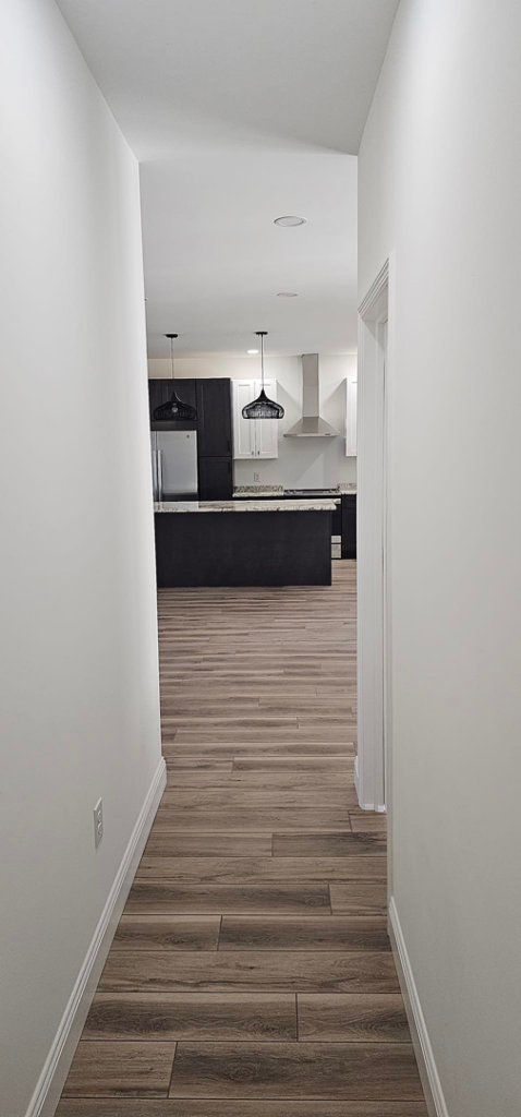 View from a hallway into a modern kitchen with dark cabinets and an island, completed by Susquehanna Valley Builders in Harrisburg, PA.