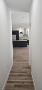 View from a hallway into a modern kitchen with dark cabinets and an island, completed by Susquehanna Valley Builders in Harrisburg, PA.