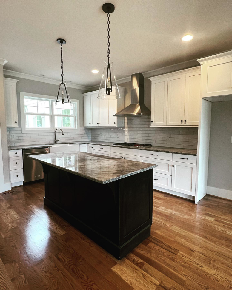 A newly installed modern kitchen with white cabinets, dark island, and stainless steel appliances by Mitchco, Inc. in Winston-Salem, NC.