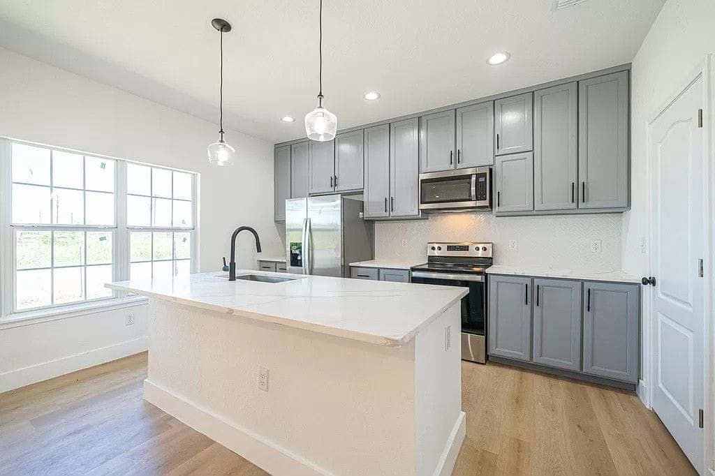 A modern kitchen renovation with grey cabinets, a white island, and pendant lighting by Morin Construction LLC in San Antonio, TX