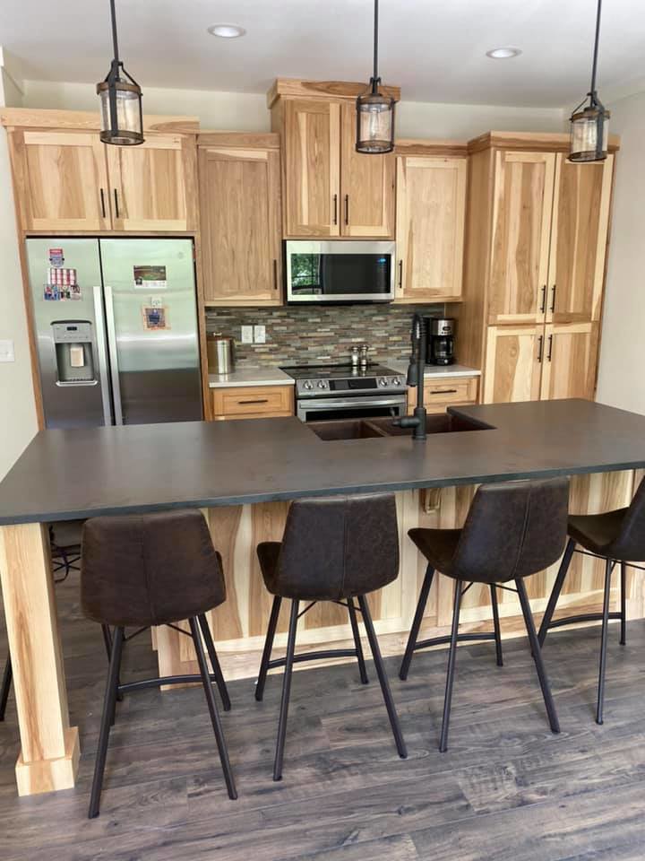 A modern kitchen featuring light wood cabinets, a dark countertop island, and bar seating by Cherokee Cabinet in Athens, GA.
