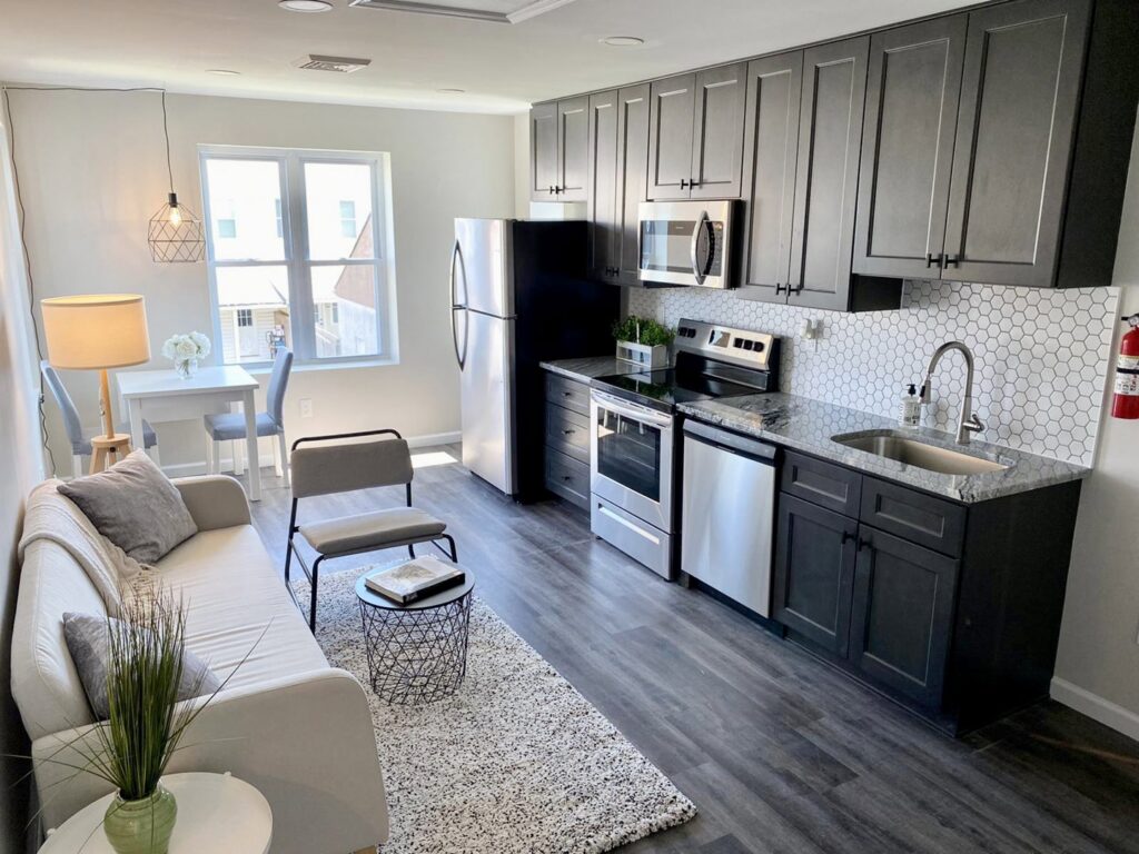 A modern kitchen and living room renovation featuring new flooring, cabinets, and a tiled backsplash by Tile Jawn in Philadelphia, PA.