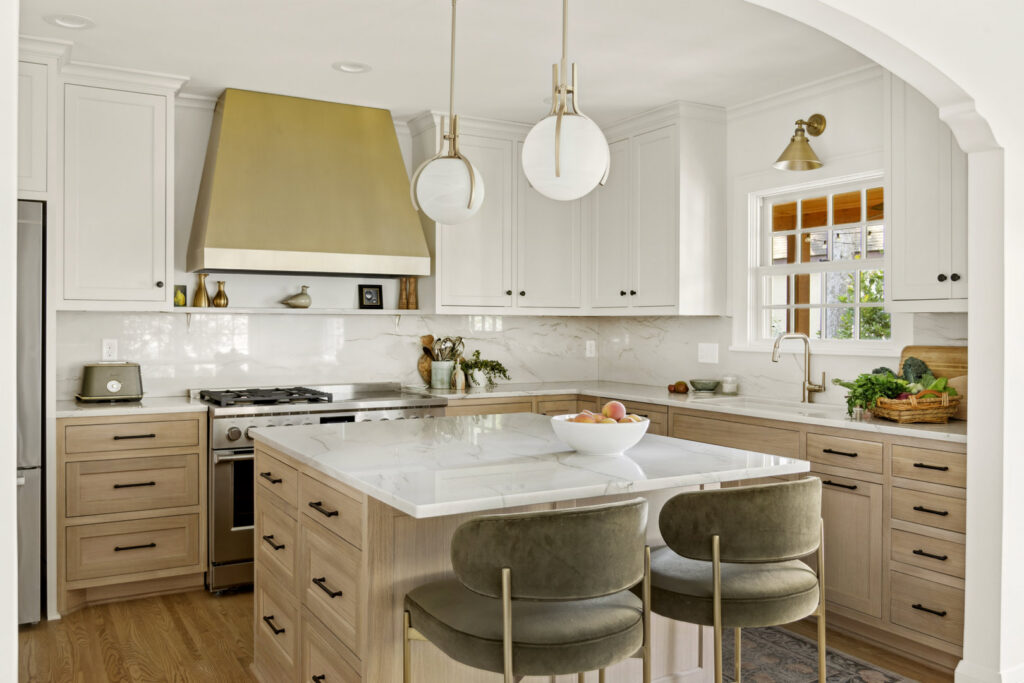 A modern kitchen remodel featuring light wood cabinets, a marble island, and a brass range hood, by Northrup Remodeling in Minneapolis, MN