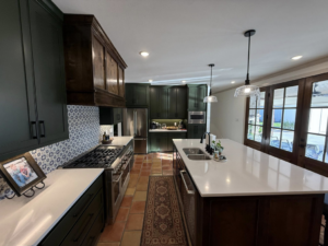 A modern kitchen remodel featuring dark green cabinets, white countertops, a decorative tiled backsplash, and a large island, completed by Javier's Painting in San Angelo, TX.