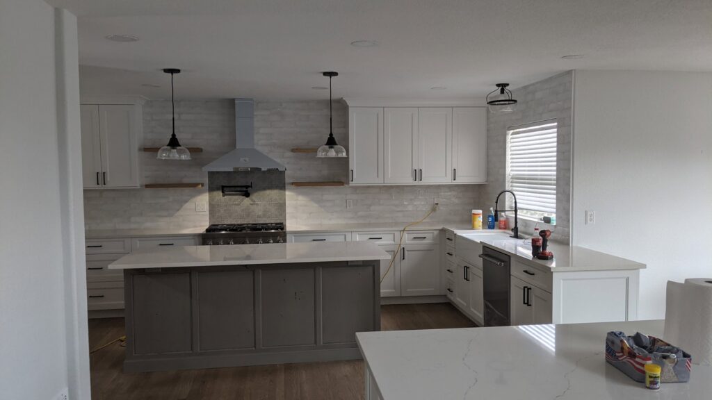 A modern kitchen remodel featuring white cabinets, a grey island, and a tiled backsplash by The Foundation Guys in Lakewood, CO