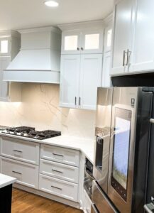 A modern kitchen remodel showcasing white cabinets, a stylish range hood, and a marble-patterned backsplash by Ruach Home Services in Laurel, MD.