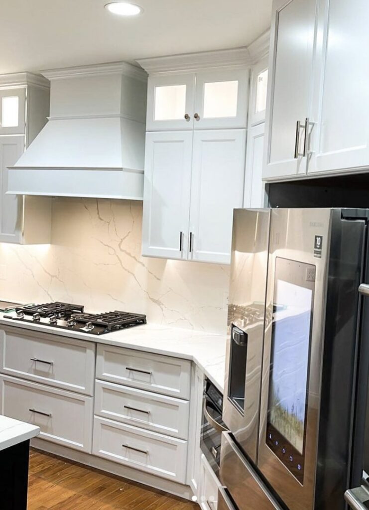A modern kitchen remodel showcasing white cabinets, a stylish range hood, and a marble-patterned backsplash by Ruach Home Services in Laurel, MD.