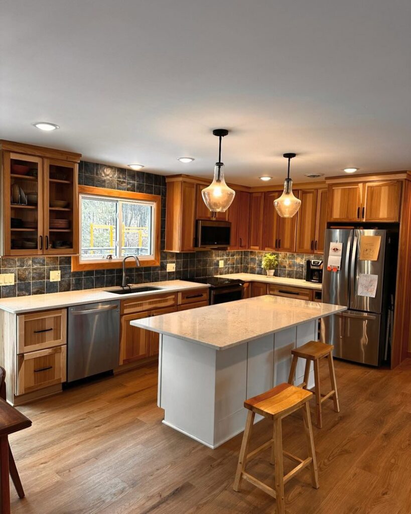 A beautifully remodeled modern kitchen featuring wood cabinets, a dark tile backsplash, and a white island with pendant lighting by Orion Construction Services in Duluth, MN.
