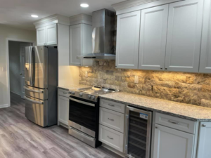 A modern kitchen renovation with light grey cabinets, stainless steel appliances, and stone backsplash by Nailed It Custom Remodeling in Chesapeake, VA.