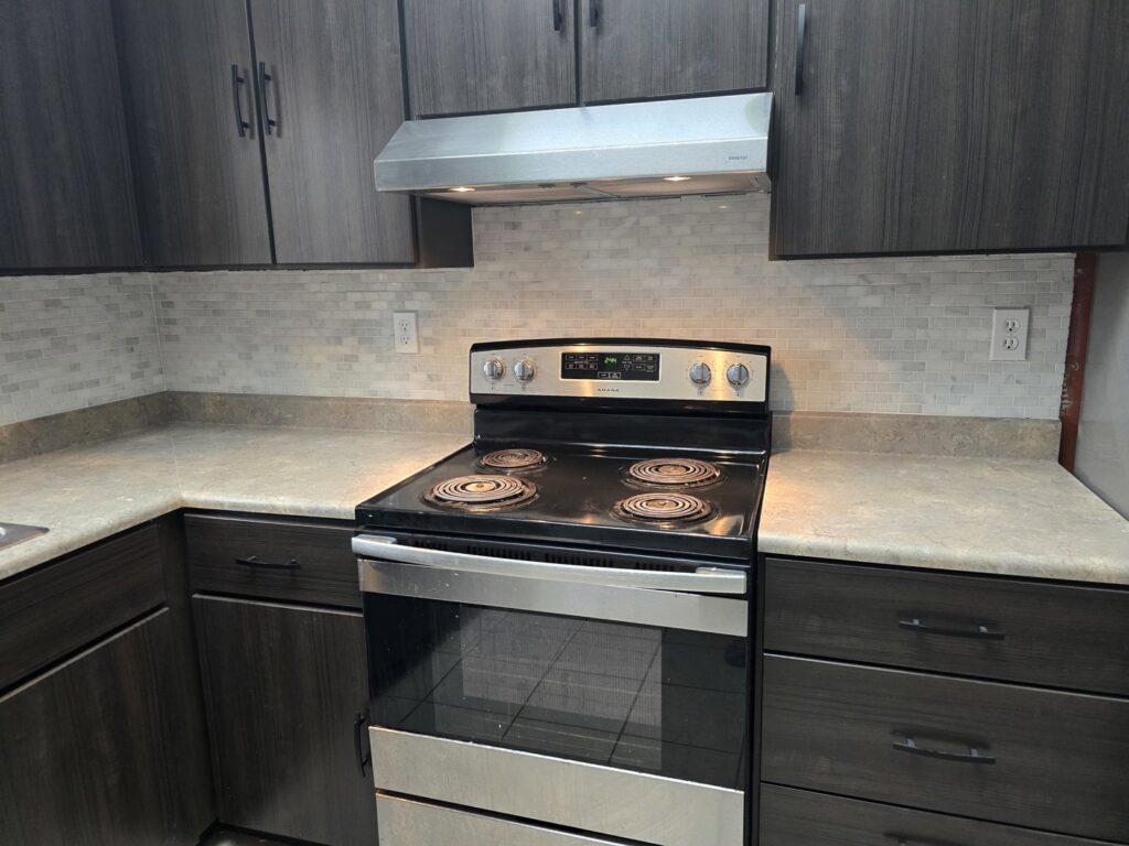 A modern kitchen renovation showcasing dark cabinets, a tiled backsplash, and a new stove by Ben Nye The Fix-It Guy in Erie, PA.