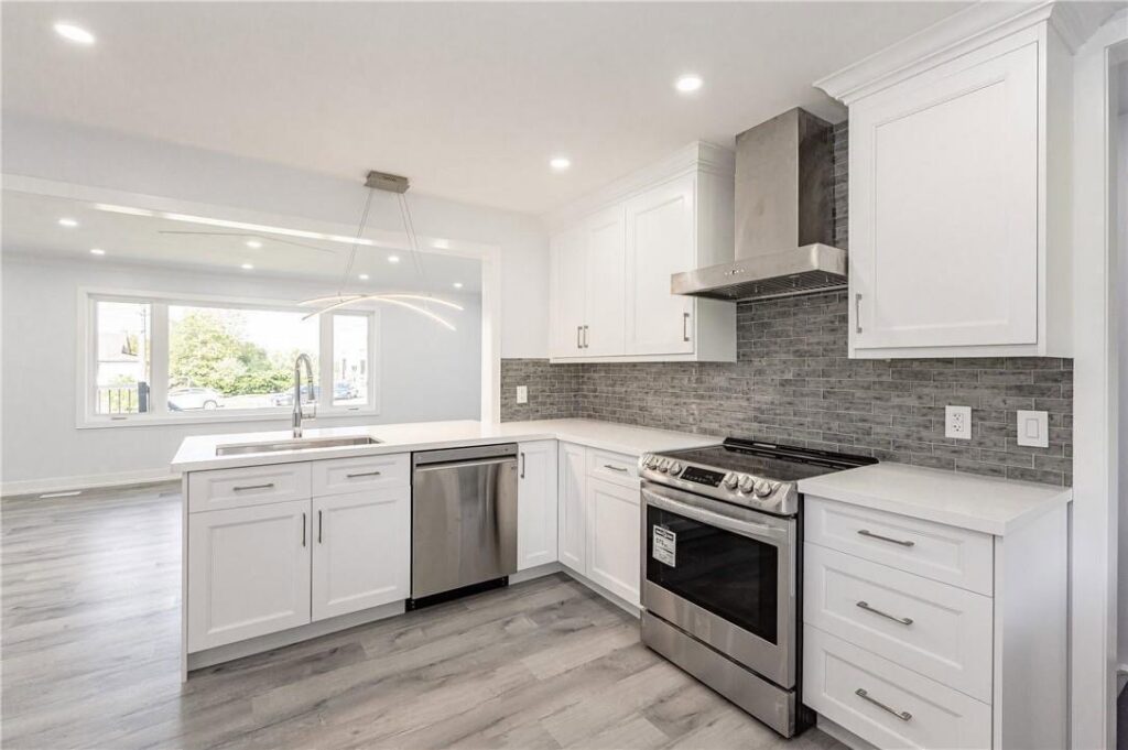 A beautifully renovated modern kitchen with white cabinets, stainless steel appliances, and a gray tiled backsplash by Men Construction in Lowell, MA.