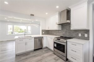 A beautifully renovated modern kitchen with white cabinets, stainless steel appliances, and a gray tiled backsplash by Men Construction in Lowell, MA.
