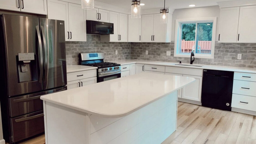 A modern kitchen renovation featuring white shaker cabinets, a large island, and stainless steel appliances by Rock Solid Construction in Rochester, NY