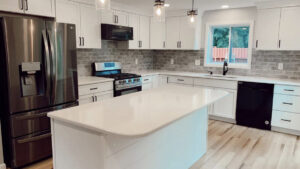 A modern kitchen renovation featuring white shaker cabinets, a large island, and stainless steel appliances by Rock Solid Construction in Rochester, NY