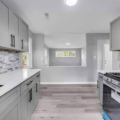 A modern kitchen renovation showcasing grey cabinets, white countertops, a tiled backsplash, and wood-look flooring by Prime Construction And Flooring in Lorain, OH.