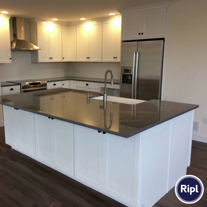 A modern kitchen with white cabinets, dark countertops, and a large island by Corrado Custom Homes, Inc. in Kutztown, PA