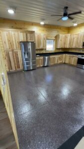 A modern kitchen with wooden cabinets and a newly installed grey flake epoxy floor by Donnelly J. LLC Epoxy in St. Charles, MO.