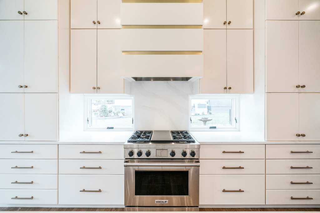 A modern kitchen featuring white cabinets, a stainless steel range, and a stylish range hood, completed by Nova Constructors in Nashville, TN.