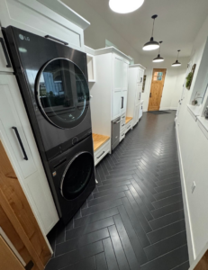 Newly installed modern laundry room with stacked washer/dryer, dark herringbone tile, and white cabinets by Fisher Construction, LLC in Selah, WA.