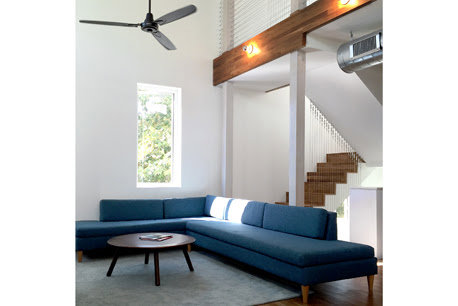 A modern living room with high ceilings, a blue sectional sofa, and a contemporary staircase by Kaleidoscope Design Build in Houston, TX.