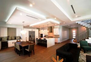A modern open-concept kitchen and living space with white cabinets and a contemporary staircase by Kornerstone Kitchens in Orlando, FL.