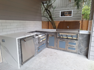 A modern outdoor kitchen with white countertops and built-in appliances by Eagle Outdoor Living LLC in Freeland, WA.