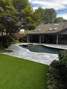 A modern swimming pool with dark tiling, grey patio, and artificial turf, a completed installation by Picasso Poolscapes in Johns Creek, GA.