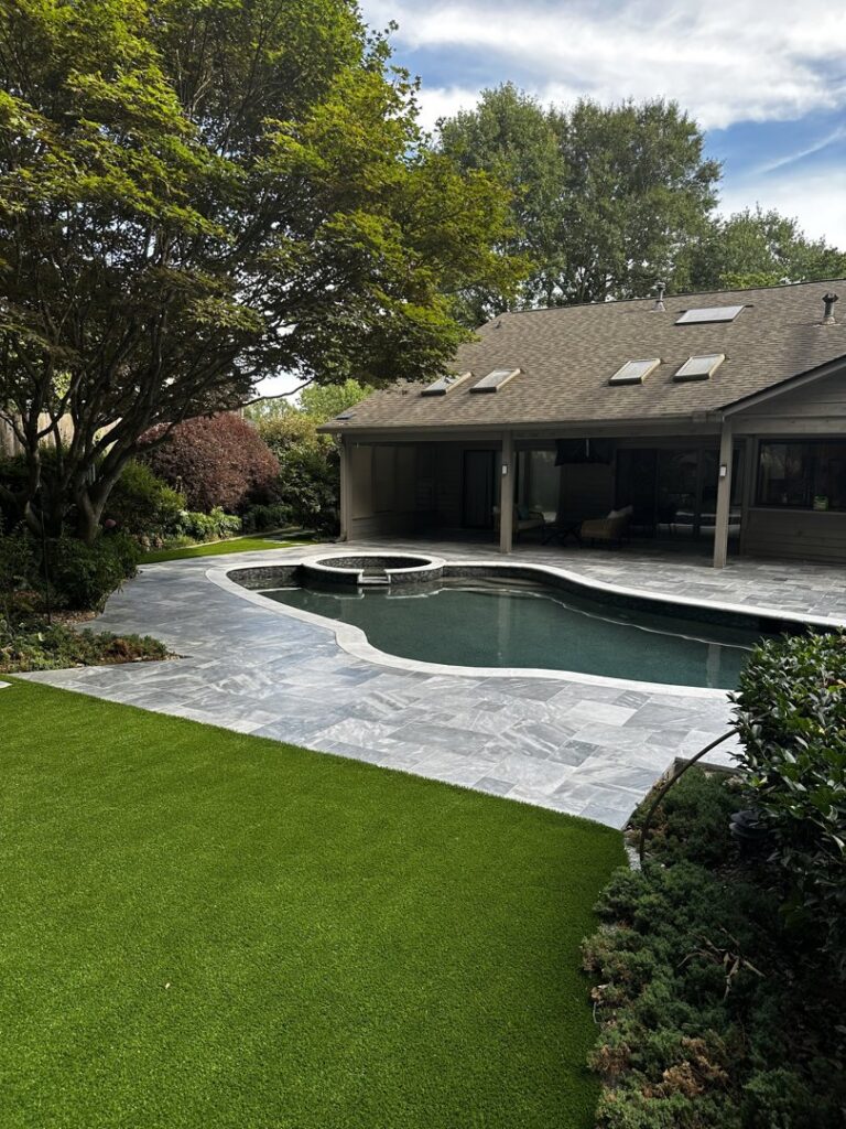 A modern swimming pool with dark tiling, grey patio, and artificial turf, a completed installation by Picasso Poolscapes in Johns Creek, GA.