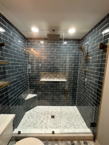 A modern shower enclosure with dark subway tiles and a clear glass door installed by Fortune Shower Doors in Sterling Heights, MI.