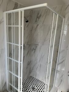 A modern shower enclosure with white grid glass and marble-look wall tiles installed by Peraza Handyman Services Llc in Bakersfield, CA.