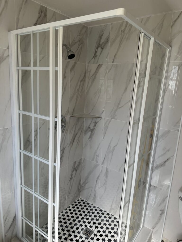 A modern shower enclosure with white grid glass and marble-look wall tiles installed by Peraza Handyman Services Llc in Bakersfield, CA.